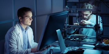 Two members from the computer engineering team working in a lab. One tech is working with a computer and one tech is fixing computer components.