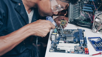 Male tech installing CPU microprocessor to the motherboard's socket on a workplace. Concepts of professional computer repair, upgrading, and servicing electronic devices with technology and computer components in an office setting.