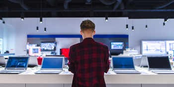 A young person stands in front of a selection of laptops to purchase. Purchasing a computer, concept.