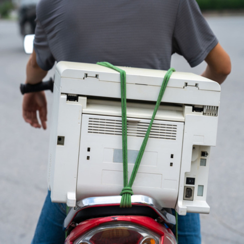 A person riding a motorbike who has a printer attached to the back of the motorbike. Donate Used Printers concept.