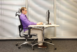 The man is seated and working on the computer, maintaining correct ergonomic posture at his workstation. This concept emphasizes proper posture on the computer.