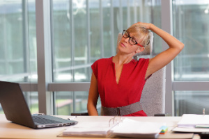 A businesswoman wearing eyeglasses is taking a short break from work in her office chair to exercise, emphasizing the importance of maintaining proper posture on the computer.