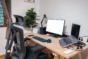 A wooden desk setup includes a laptop, display, mouse, lamp, ergonomic chair, and artificial tree. The concept represents setting up a home office.